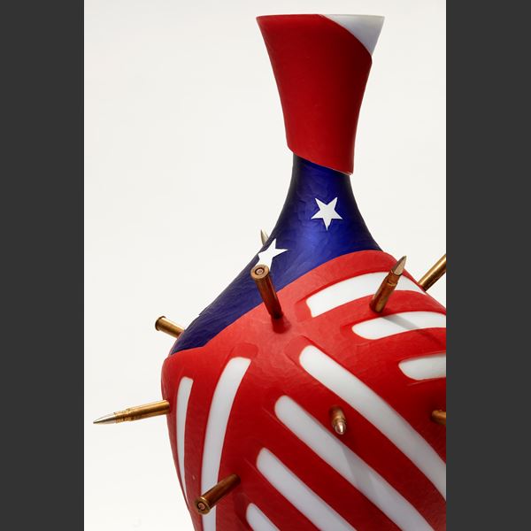 red white and blue amphora bottle with abstract stars and strips pattern pierced with bullets with a black metal stand