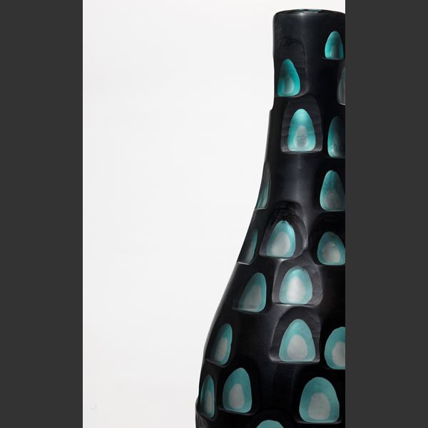 tall elongated bottle form with cut out rounded detail like an abstract peacock feather in black and jade hand made from glass with metal stand