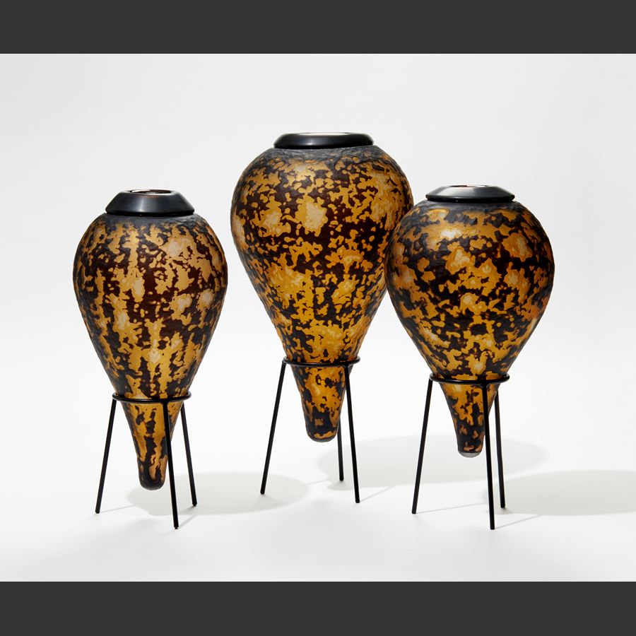 amber and black teardrop bottle with textured organic cut surface sat on a black tripod museum style stand