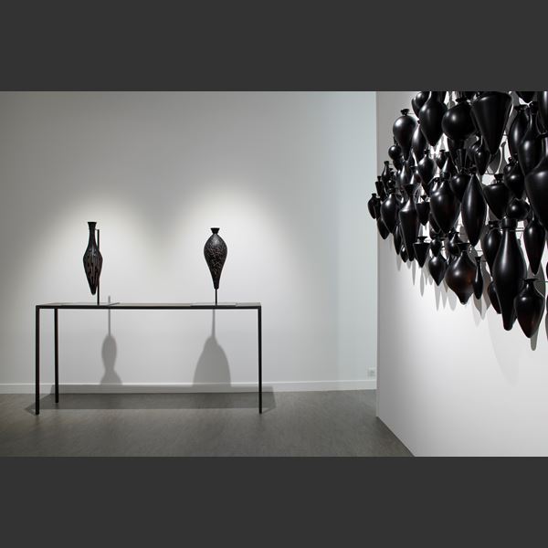 hundreds of black handblown and polished small amphora bottles wall mounted and hung in a clustered pointed horizontal oval configuration