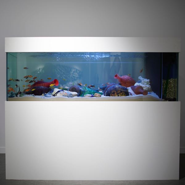 large rectangular fish tank with base covered in sand with nestled discarded colourful handblown textured glass amphora bottles with real fish swimming amongst them 