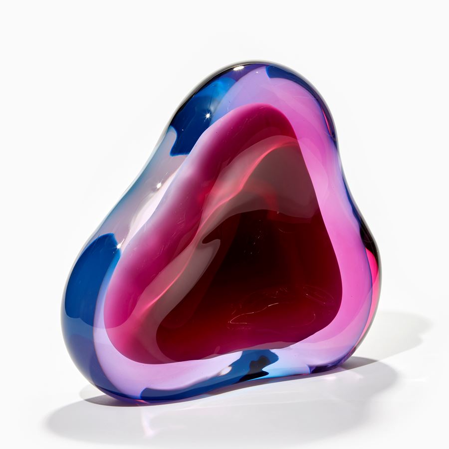soft fluid triangular standing shape with interior cavity lined in brilliant white that is surrounded in transparent layers in turquoise and pink which merge creating further hues handmade from glass