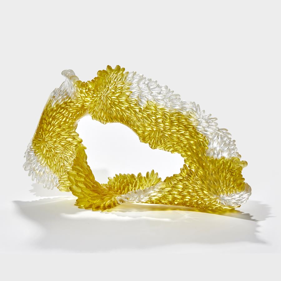 soft squat textured organic rough oval standing form in white and gold yellow with one side shiny the other textured with raised scales hand made from cast glass 