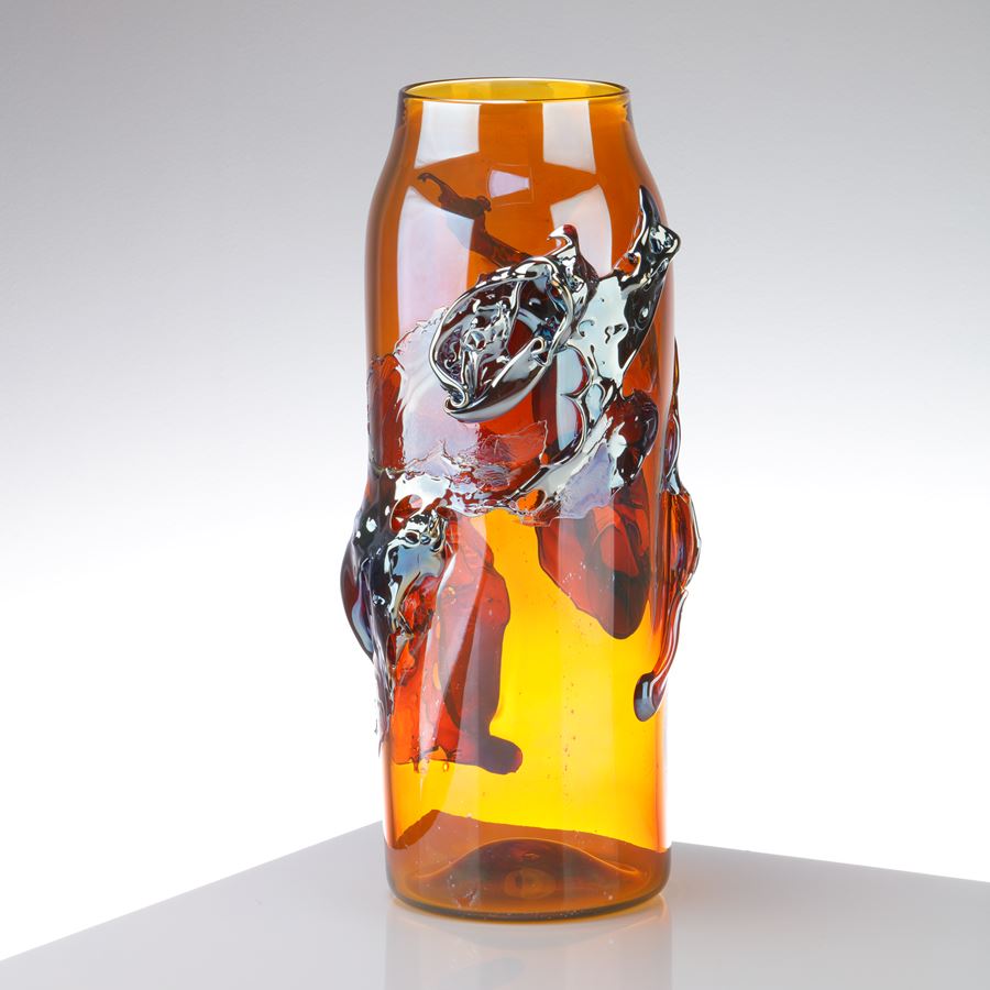 brilliant transparent amber cylindrical vase with tapering neck with roushed organic textural raised detail in metallic blue and lilac handmade from glass