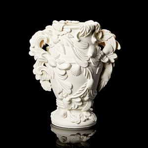 off white slightly bulbous vessel with flared foot ring covered in baroque flourishes swirls and shells with two handles equally adorned hand made from porcelain