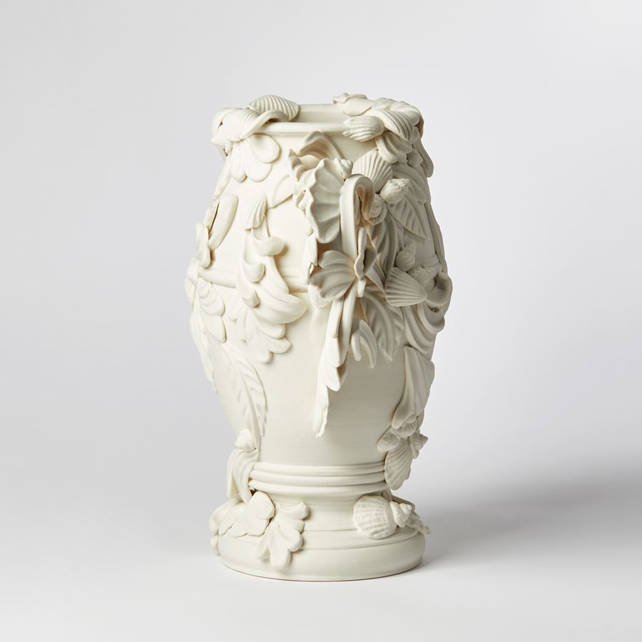 off white slightly bulbous vessel with flared foot ring covered in baroque flourishes swirls and shells with two handles equally adorned hand made from porcelain