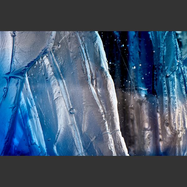 transparent angular sculpture with rugged cliff face detail with areas in light and dark blue hand made from cast glass