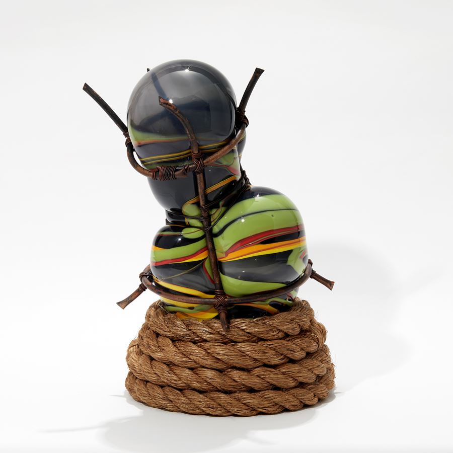 hand blown glass bulbous sculpture in grey and mixed banded african colours of red yellow and green with wound rope base and set within a copper cage