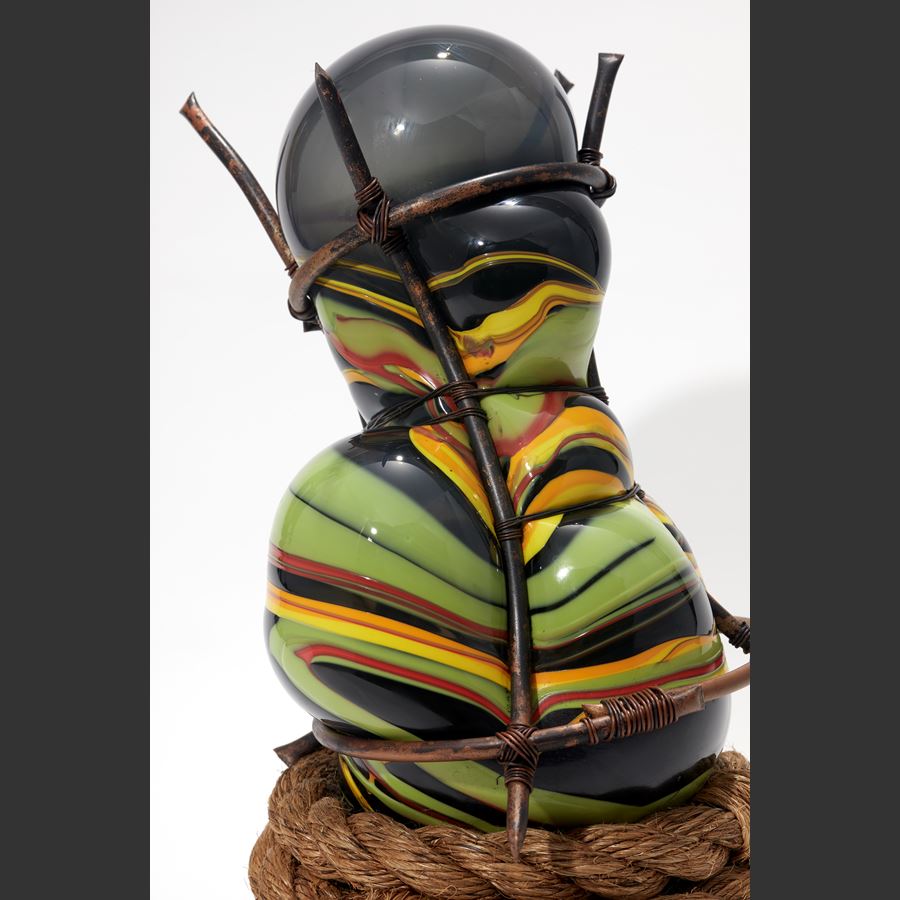hand blown glass bulbous sculpture in grey and mixed banded african colours of red yellow and green with wound rope base and set within a copper cage