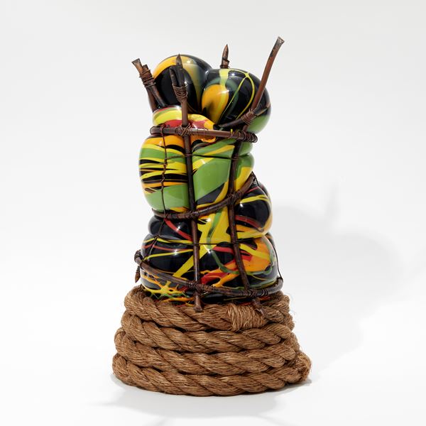 hand made glass sculpture blown in to a copper cage with the appearance of bursting through in black orange green and yellow with coiled rope base