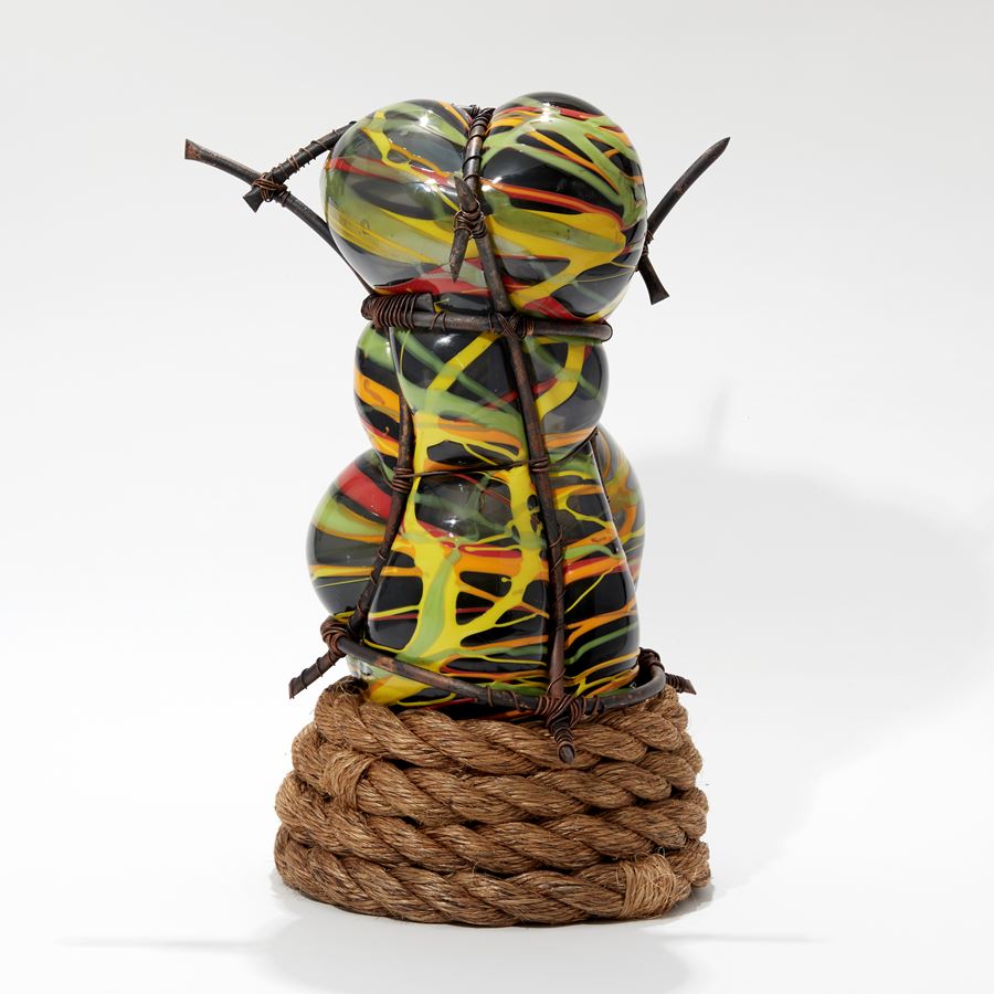 abstract figurative sculpture in grey with splashed lines in orange yellow and green set within a copper cage  with a coiled rope base