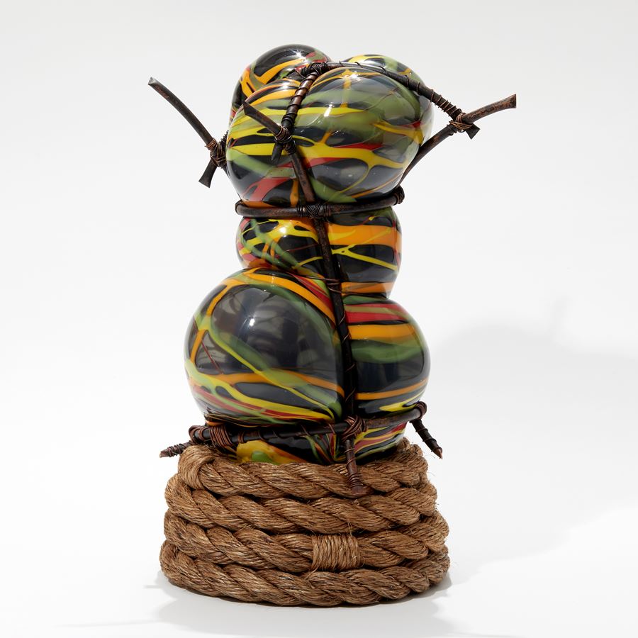 abstract figurative sculpture in grey with splashed lines in orange yellow and green set within a copper cage  with a coiled rope base