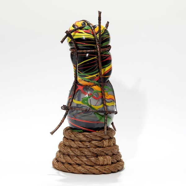 coiled rope base with bulbous abstract figure on top in black yellow red orange and green held within a copper cage handmade from glass