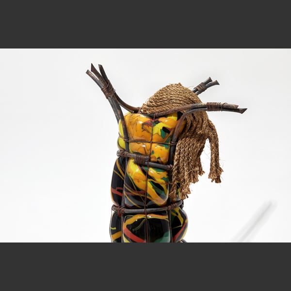 tall glass figure in black yellow orange red and green held within copper bars with rope mask and coiled rope base