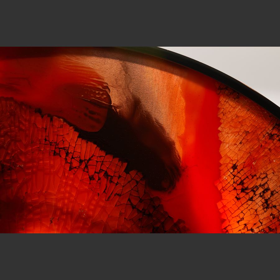 black round metal frame with solid rectangular base holding an abstract red orange and black glass artwork based on the evil amulet hand made from shattered and sheet glass