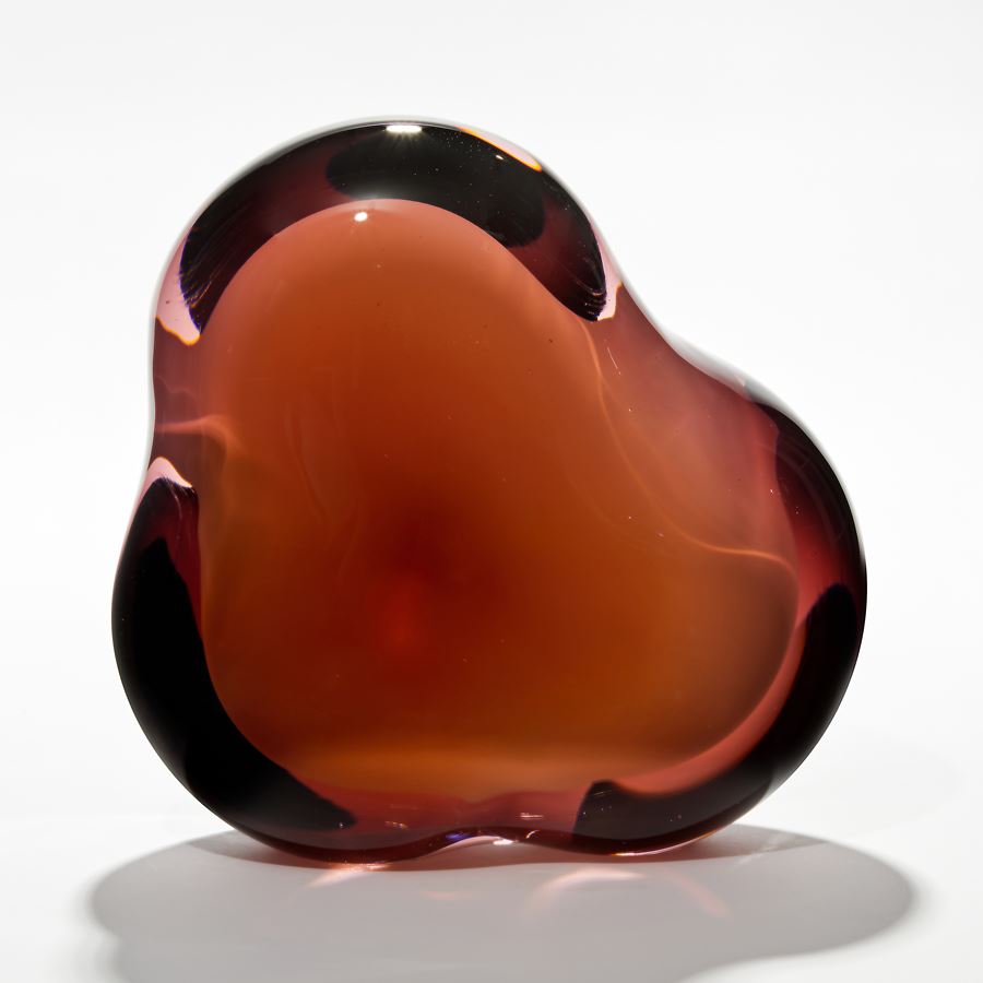 amorphous sculpture with opaque white central hole surrounded by transparent layers in dark amber peachy brown hand made from glass