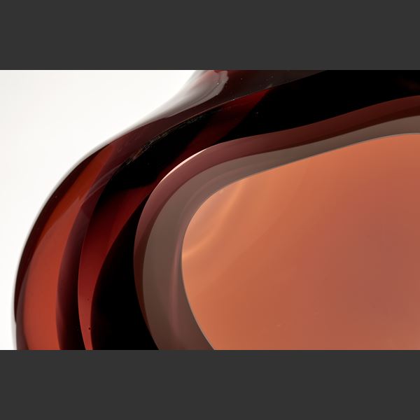 amorphous sculpture with opaque white central hole surrounded by transparent layers in dark amber peachy brown hand made from glass
