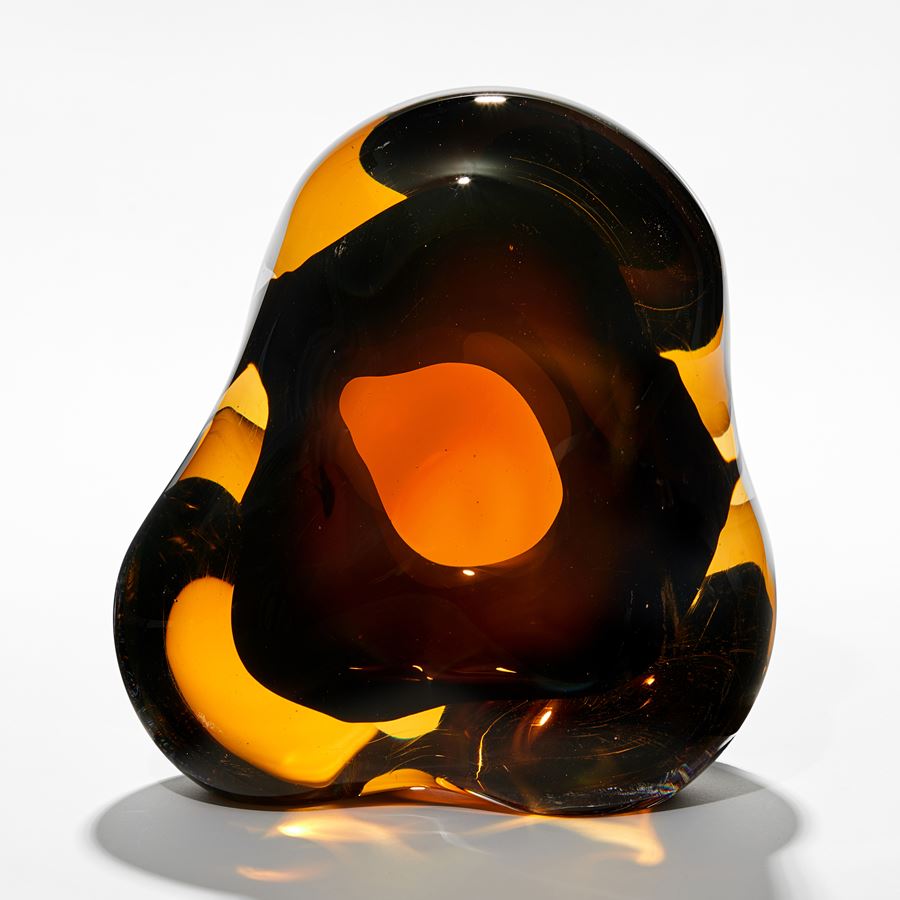 rounded amorphous sculpture created from transparent layers of bright amber and rich brown with a darker centre and organic middle hole hand made from glass