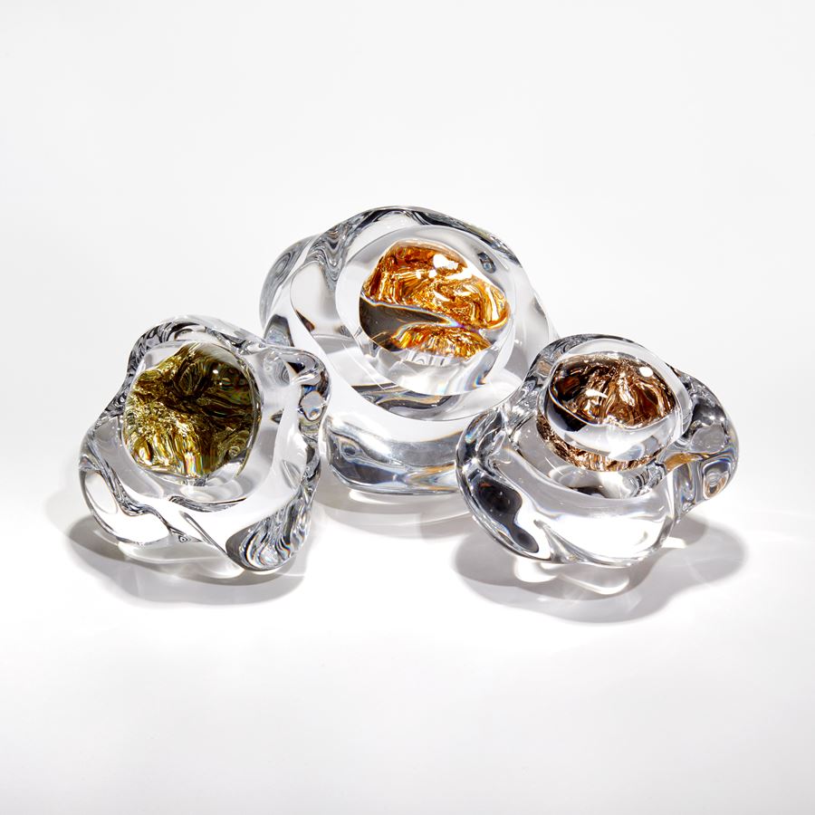 clear amorphic rock with smooth surface with densely packed champagne gold leaf trapped inside with the view warped due to the exterior mass acting as a lens hand made from glass