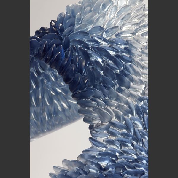 hand made standing textured looping sculpture in cast glass with scaly front surface and a polished back surface in indigo blue soft grey and clear glass