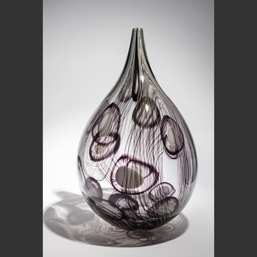 transparent grey and aubergine teardrop shaped vessel with fine lines and abstract circle patterns in dark aubergine handmade from glass