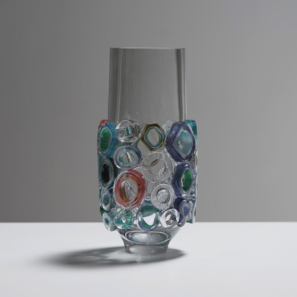 transparent tubular vase with lower half covered in raised sections in various shaped rings with different colours and patterns hand made from blown glass