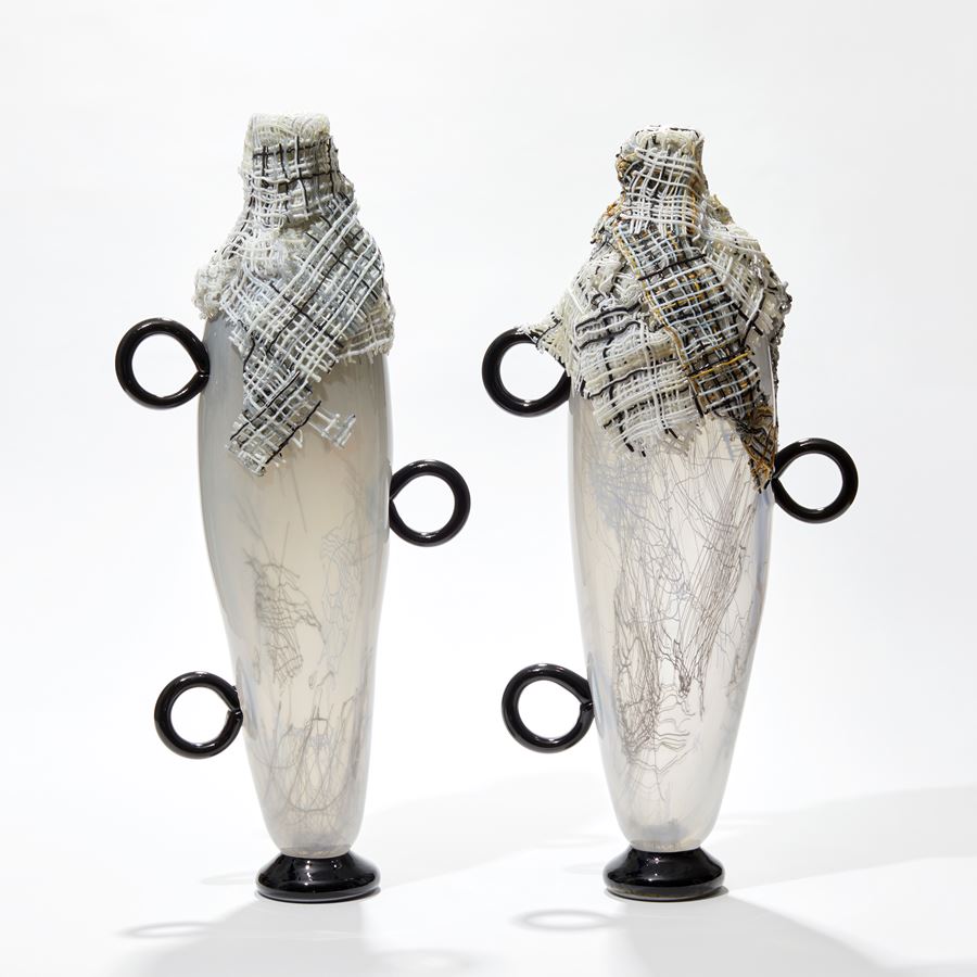 tall opaque white abstract figurative vessel with black ring handles and wrapped in multi-coloured cloth round the opening hand made from glass