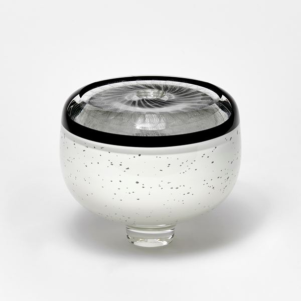 round vessel with small top opening in black and white with speckled base upper black band and white swirling patterning on the top flat surface hand made from glass