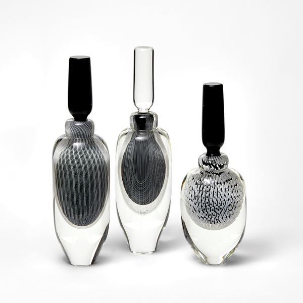 tall elegant round clear bottle with tapered base and long black stopper with fine filigree pattern trapped within hand made from glass