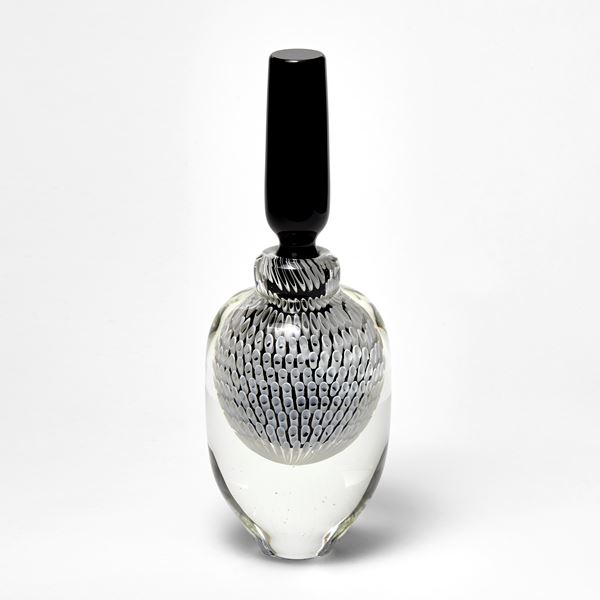 clear round bottle with tapering base with long black stopper with black and white tubular pattern trapped inside hand made from glass