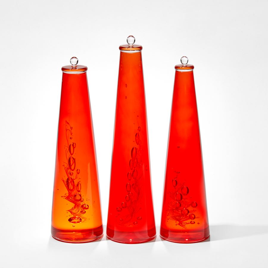 trio of bright red conical solid bottles containing trapped bubbles and a whirling helix hand made from glass