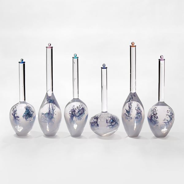 five glass bottles with bulbous white bottoms fading to clear in their long thin necks each containing a blue helix line detail and all with coloured stopper in different colours