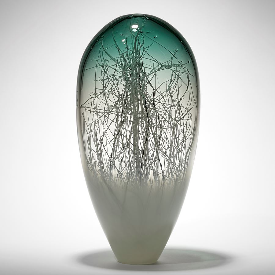 upside down teardrop shaped abstract sculpture with transparent jade green top fading to clear then soft  hazy opaque white with erratic thin tangled canes in black and white trapped inside hand made from glass