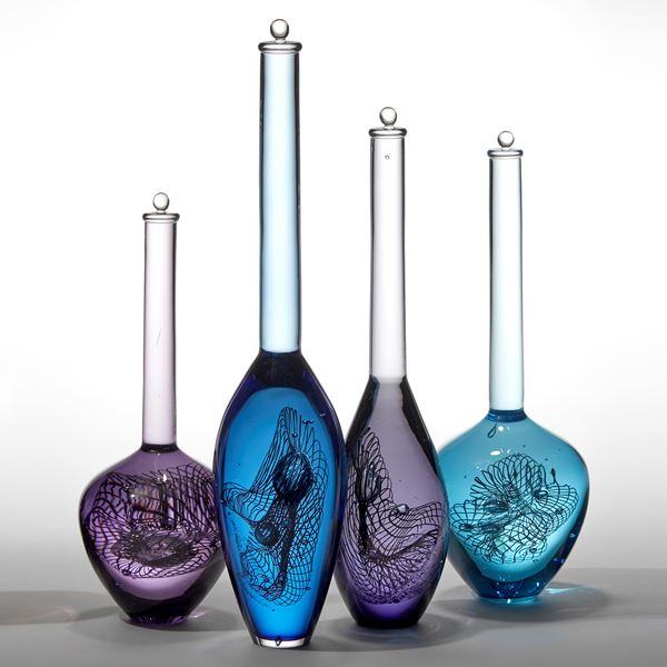 installation of nine solid transparent bottle forms in blue purple and jade each with a long tall neck with stopper capped top and a rounded bottom section containing a double helix hand made from glass 