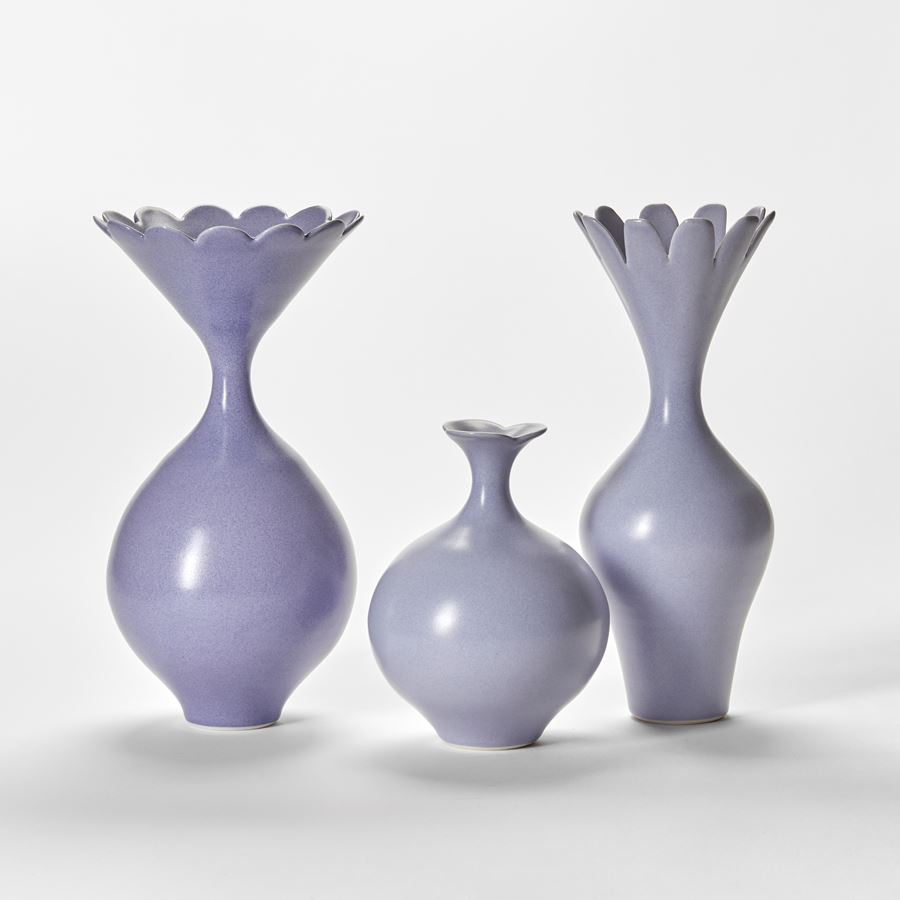 set of three porcelain vases in soft mauve purple each with a flared top neck with simple floral scalloped edges