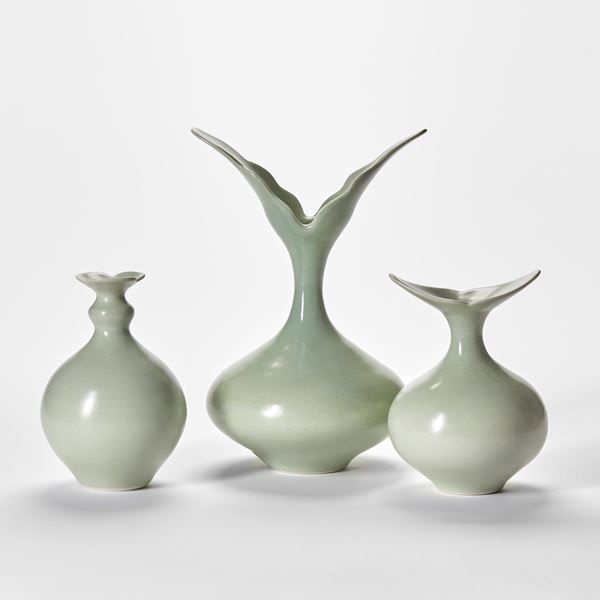 three soft green hand thrown porcelain vases with rounded bases and narrowing necks and flared openings with simplified petal floral details