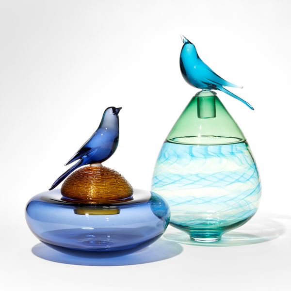 lime green and blue teardrop shaped bottle with swirling pattern and upper top section in transparent green with stopper and blue bird perched on top hand made from glass