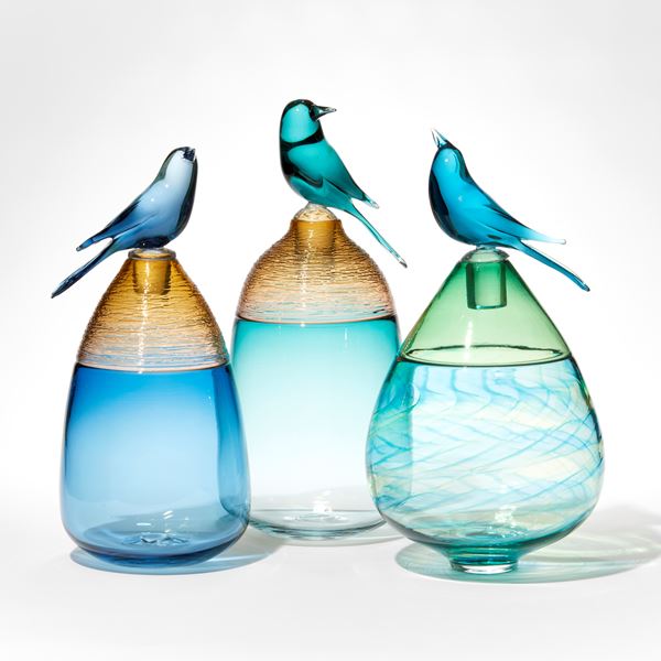 lime green and blue teardrop shaped bottle with swirling pattern and upper top section in transparent green with stopper and blue bird perched on top hand made from glass