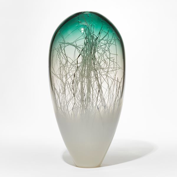 upside down teardrop shaped abstract sculpture with transparent jade green top fading to clear then soft  hazy opaque white with erratic thin tangled canes in black and white trapped inside hand made from glass