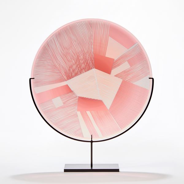 transparent grey and soft pink rondel made from blown glass with etched surface with geometric pattern presented on a black steel stand