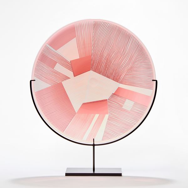 transparent grey and soft pink rondel made from blown glass with etched surface with geometric pattern presented on a black steel stand