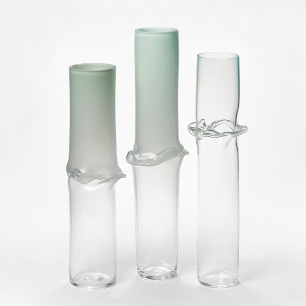 tall cylinder with transparent clear bottom half and opaque celadon green top half with central creased and slumped rippling and bulging waist hand made from glass
