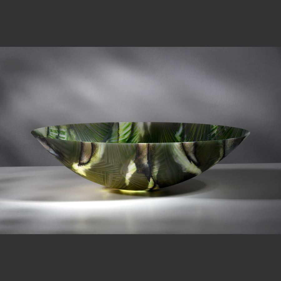 oval bowl with sweeping sides and rounded base with palm tree interior repeat pattern and exterior camouflage pattern in a myriad of greens hand made from glass