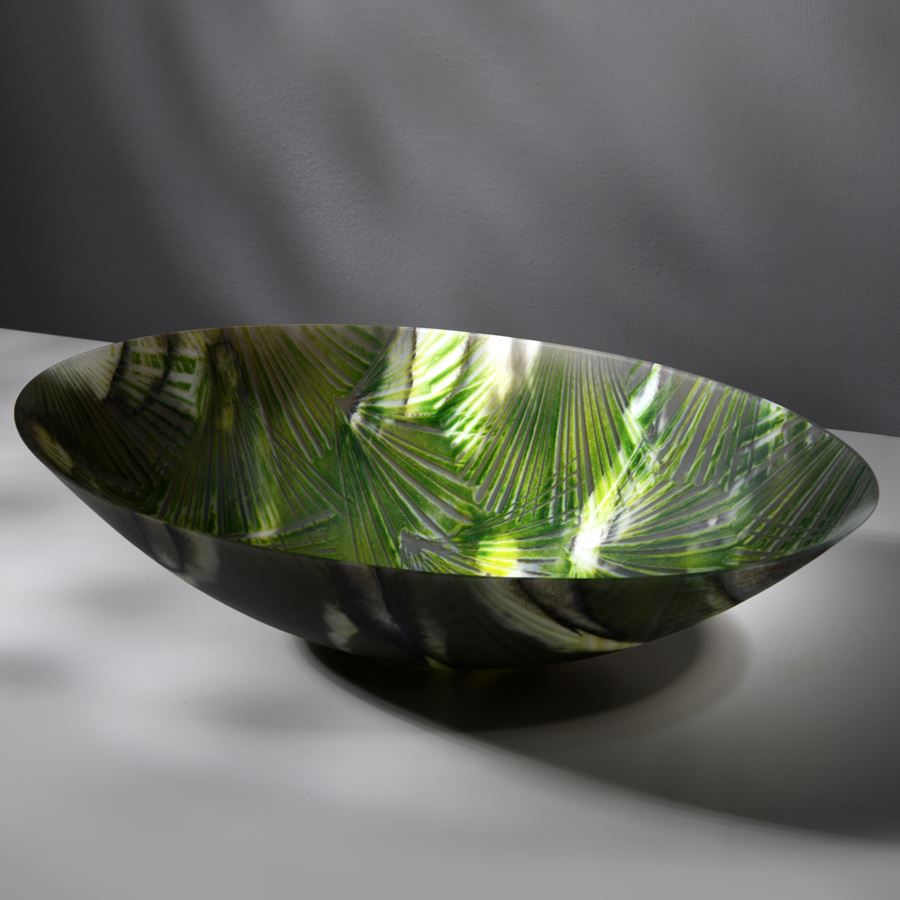 oval bowl with sweeping sides and rounded base with palm tree interior repeat pattern and exterior camouflage pattern in a myriad of greens hand made from glass