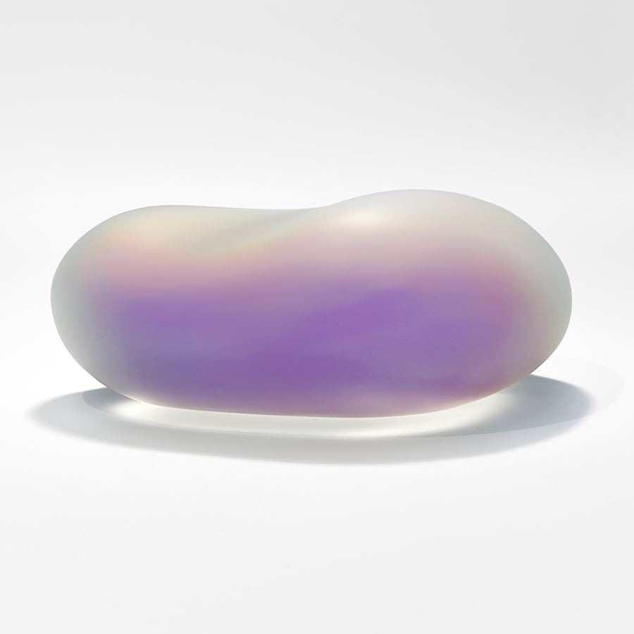 large smooth surfaced rock sculpture made from cast opaque glass with a trapped film inside giving off the effect of dragonfly wing colours creating a shimmering rainbow of all different hues