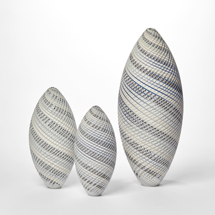 tall standing ovoid vessel with small opening at the top and curling lines round the form in white grey and soft blue with textured cut surface hand made from glass