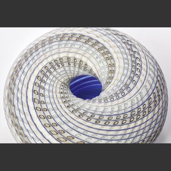round vessel in soft blue off white blue and green with swirling lines to the dipped vortex centre with lines both coloured and cut within the surface handmade from glass