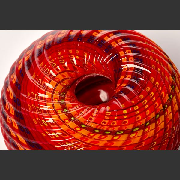 round textured orange yellow and aubergine purple striped vessel with central dipped opening with straight cut recessed lines swirling around the piece hand made from glass