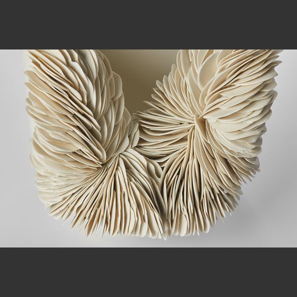 ivory coloured round bowl with tall sides and front third cut away with the gap filled with stacked shards hand made from porcelain