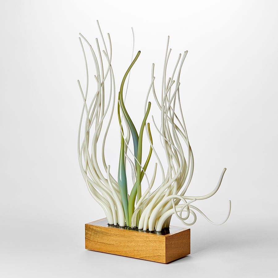 wooden rectangular base with profusion of upwardly undulating glass canes in soft green mint alabaster white and teal  which appear to be moving as if under water